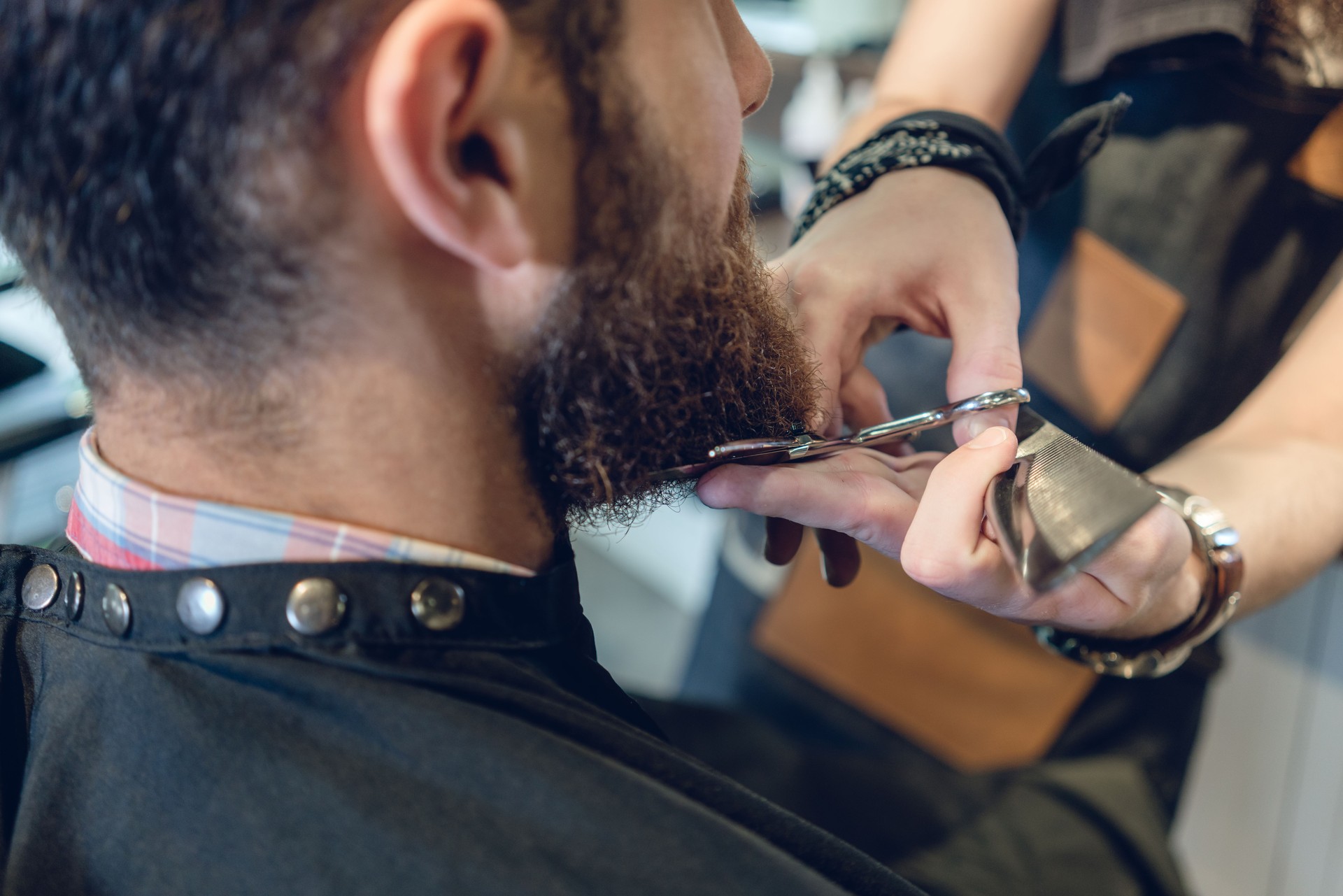 Close-up of the head of a young man and the hands of a hairstylist trimming his beard